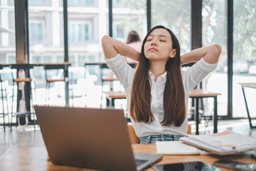 Stressed office worker takes a moment to relax and stretch at her desk in a bright, modern...