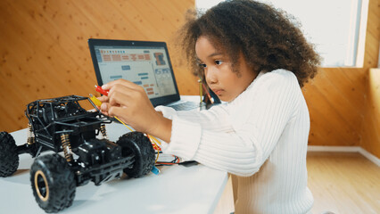 Smart african girl build robotic car while using wires while using laptop setting or writing prompt...