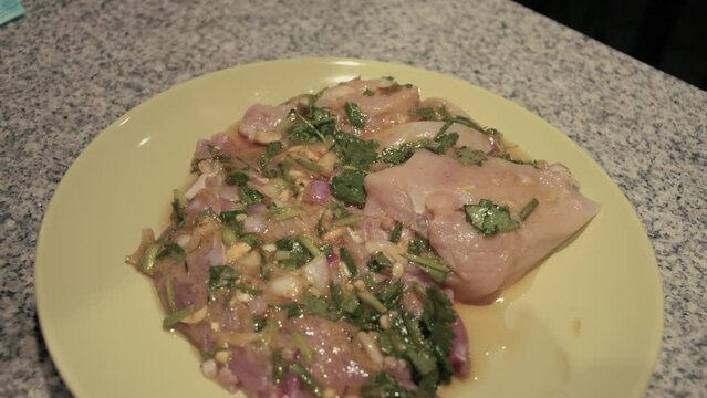 March 3, 2024 - Toronto, Ontario Canada. Close up demonstration of placing a plate of cut, marinating chicken on a counter.