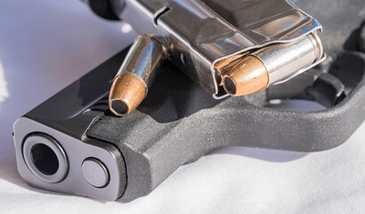 A loaded 9mm pistol magazine on a black 9mm pistol with a single hollow point bullet stacked together on a white background
