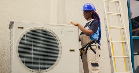 Efficient repairman starting work on defective air conditioner, using handheld drill to disassemble...