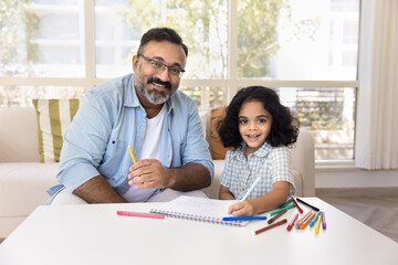 Happy caring Indian granddad and sweet granddaughter girl drawing in colored pencils at home...