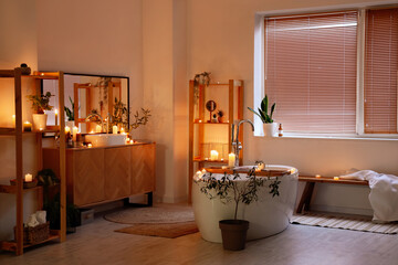 Interior of bathroom with burning candles, sink and shelf units in evening