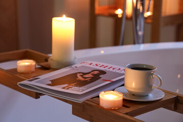 Obraz na płótnie Canvas Coffee cup with magazine and burning candles on bathtub in evening, closeup