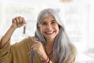 Happy retired elderly Latin woman showing keys from new home, smiling, promoting mortgage, rent...