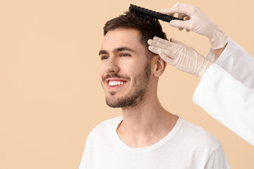 Doctor brushing young man's hair on beige background, closeup