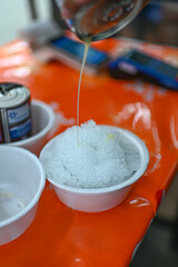 Shaved ice is being poured with white milk into a white bowl