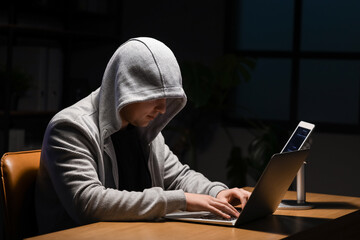 Hacker using laptop at table in dark room