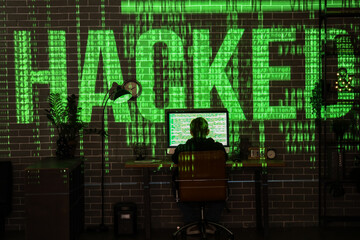 Obraz premium Hacker using computer at table and projection of word HACKED in dark room