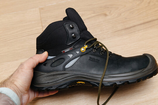 Hamburg, Germany - Feb 16, 2022: POV male hand looking at new Safety shoes S3 HRO WR SRC Hydro Modytex high black - wooden parquet background