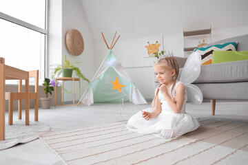 Cute little girl dressed as fairy with magic wand at home