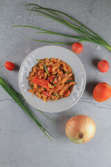 Macaroni in tomato sauce with fresh tomato and onion in white plate. Top view, horizontal composition. Popular italian food.
