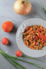 Macaroni in tomato sauce with fresh tomato and onion in white plate. Top view, horizontal composition. Popular italian food.
