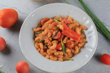 Macaroni in tomato sauce with fresh tomato and onion in white plate. Top view, horizontal composition. Popular italian food.