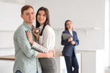 Happy young couple with keys from their new flat hugging in kitchen