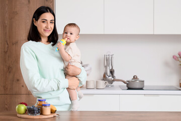 Mother giving her little baby nibbler with food in kitchen