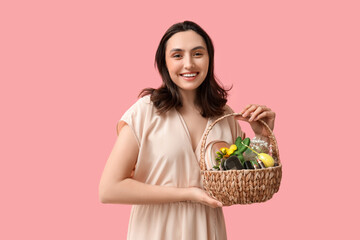 Happy young woman holding Easter basket with decorative cosmetics on pink background