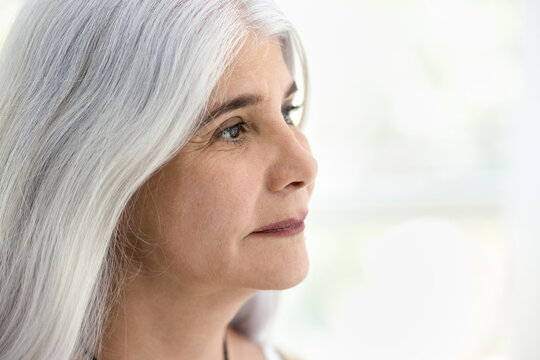 Face of calm positive old retired woman with natural make up and long grey haired looking at copy space away, thinking on elderly beauty care, skincare, dreaming. Close up casual portrait