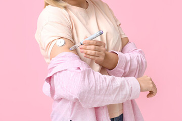 Woman with glucose sensor for measuring blood sugar level and lancet pen on pink background....