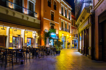 Fototapeta na wymiar Cafes and shops colorfully illuminated at night in the central Barrio Santa Cruz district of the Andalusian city of Seville, Spain.