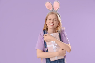 Young girl with Easter bunny ears and gift on lilac background