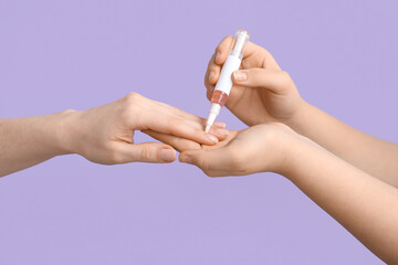 Female hands applying cuticle oil with pen on lilac background, closeup