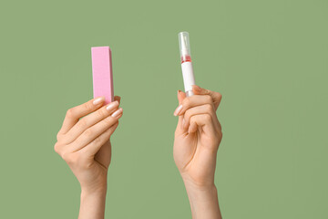 Female hands with cuticle oil pen and nail buffer on green background