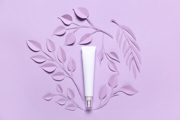 Tube of cosmetic product, paper flowers and leaves on color background