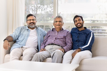 Happy young adult Indian grandson and son spending leisure time with older grandpa and mature...