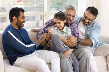 Happy young adult Indian father, grandpa, great granddad playing with sweet little preschool kid...