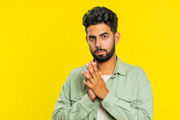 Sneaky cunning Indian young man with tricky face gesticulating and scheming evil plan, thinking over devious villain idea, cheats, jokes, pranks. Arabian Hindu guy isolated on yellow studio background - obrazy, fototapety, plakaty