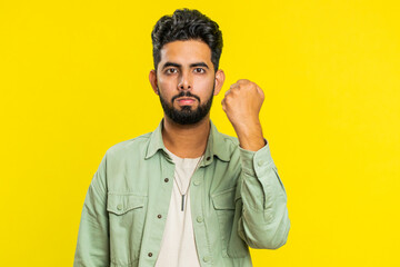 Aggressive angry Indian young man trying to fight at camera, shaking fist, boxing with expression, punishment, threaten, bullying, abuse, mad fury. Arabian guy isolated on yellow studio background - obrazy, fototapety, plakaty