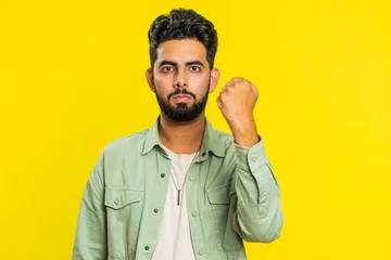 Fotobehang Aggressive angry Indian young man trying to fight at camera, shaking fist, boxing with expression, punishment, threaten, bullying, abuse, mad fury. Arabian guy isolated on yellow studio background © Andrii Iemelianenko