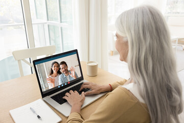 Happy young married couple talking to senior mom on video call, waving hands from laptop screen,...