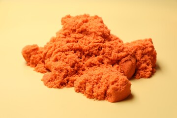 Pile of orange kinetic sand on beige background, closeup
