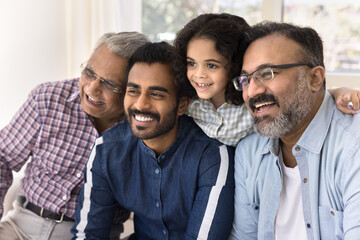 Happy Indian family four generations meeting and laughing, posing at home, looking away with toothy...