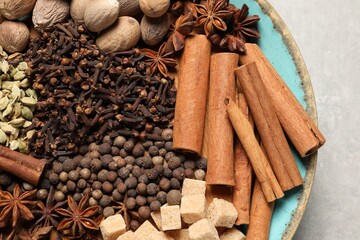 Different spices and nuts in bowl on light gray table, top view