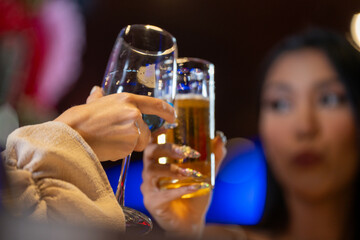 close up glasses of clinking glasses of champagne with lighting. Dinner party with drinking of champagne. hands holding clear glass with alcohol in yellow shine reflect.
