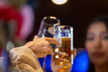 close up glasses of clinking glasses of champagne with lighting. Dinner party with drinking of champagne. hands holding clear glass with alcohol in yellow shine reflect.