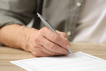 Senior man signing Last Will and Testament at wooden table, closeup