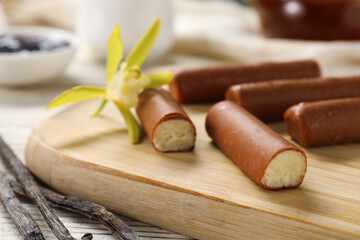 Glazed curd cheese bars, vanilla pods and flower on white wooden table, closeup