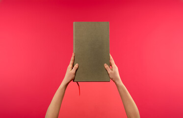 hands holding a book on a pink background - 750270396