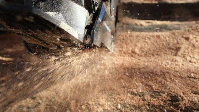 Slow motion and close up shot of sawdust flying toward lens while using gas chainsaw to cut oak stump or log into smaller pieces.