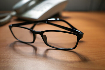 A black eyeglasses and an old landline telephone on wood table, shallow focus