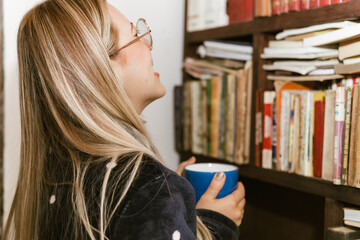 Book Day, April 23rd. Blonde woman with glasses reading a book while drinking chocolate.