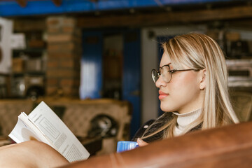 Book Day, April 23rd. Blonde woman with glasses reading a book in her living room. Tranquility.
