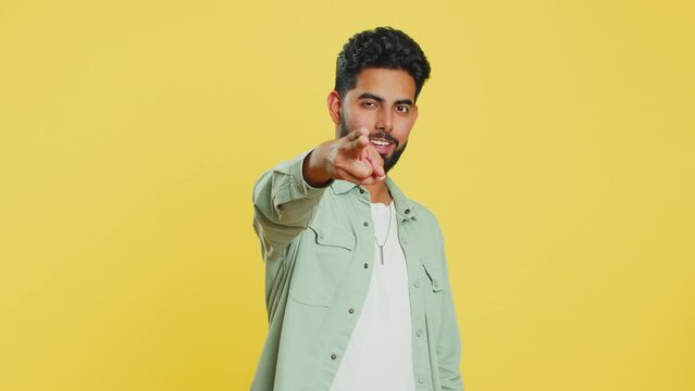Call me, here is contact number. Indian man looking at camera doing phone gesture, asking for conversation. Hotline online service proposition advertisement. Arabian guy isolated on yellow background