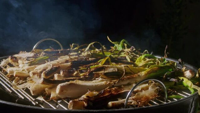Traditional Spanish catalan green winter onion calcots, spring green season grill barbecue, vegan bbq with fire in Barcelona, Catalonia. Close up of grilling green onion.