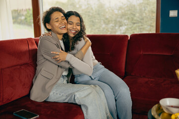 Obraz premium Smiling female friends hugging and enjoy time spent together while sitting on sofa during home party