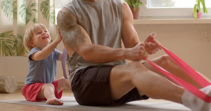 Fit father kisses his child. Integration of family bonding and physical activity during home workout session. Including loved ones in fitness routines and nurturing familial relationships. Cozy home.